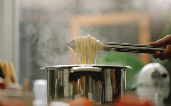 a person cooking the spaghetti with a ss soup pan